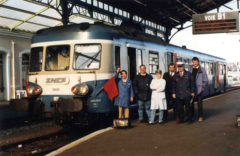 Gare d'Aurillac : de gauche à droite, Gaston Laffaille levant le poing, Jean-Claude Cornibert, Denise Valat, Didier Bonal, Gérard Conrié et Rémy Maury, prenant la pose devant l'autorail orné des drapeaux rouges