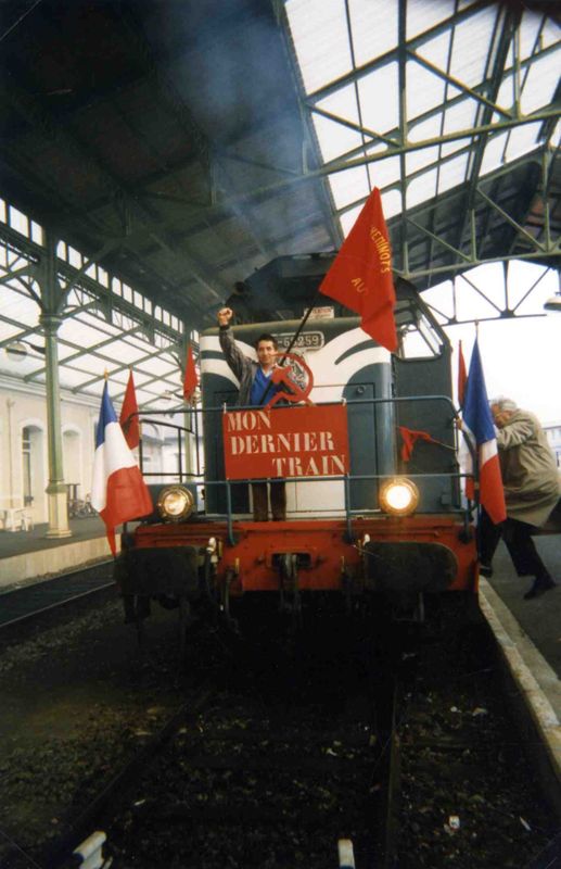 Gare d'Aurillac : Gaston Laffaille prenant la pose à l'avant de la locomotive poing levé et drapeau rouge des cheminots du parti communiste aurillacois à la main ; tandis que Louis Taurant (ancien secrétaire général du parti) monte le rejoindre